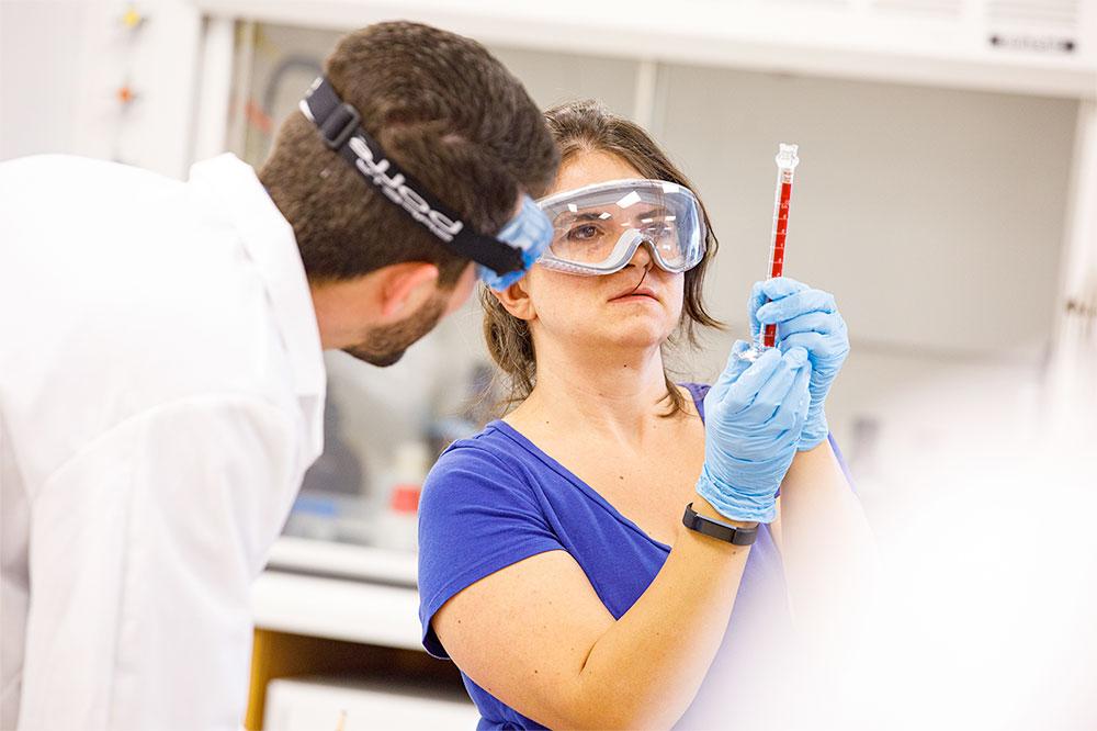 A student taps a beaker during a chemistry experiement while their Frostburg professor observes